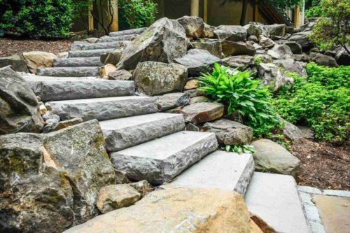 Thick natural stone slab steps surrounded by boulders and greenery.